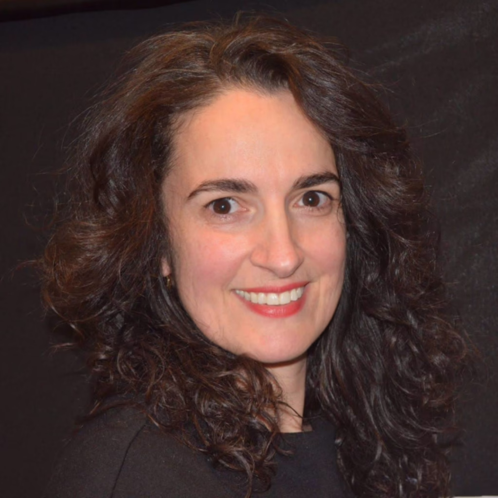 Head-and-shoulders portrait of a smiling woman with dark, curly hair against a dark background.